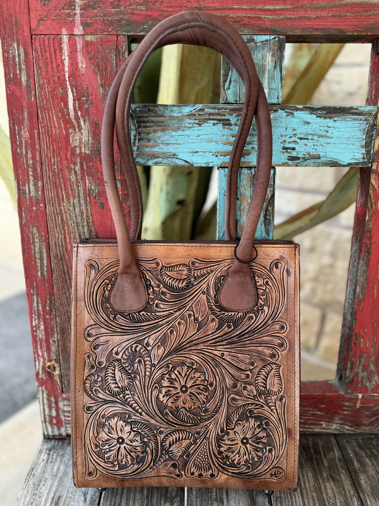 ADBGZ456 — Women's rich tan genuine leather structured tote purse with deep full-coverage floral and scroll hand-tooling, large central daisy/sunflower motif with sweeping acanthus leaf scrollwork and dark brown antiqued contrast, and two sturdy dark brown rounded loop leather top handles — Blair's Western Wear Marble Falls TX
