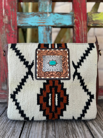 ADBGA286D — Women's handbag with a bold cream and black Navajo-inspired geometric woven front panel with rust/burnt orange accent details, square hand-tooled floral leather frame with silver scalloped oval concho and turquoise oval stone center, brown leather sides, and adjustable tooled leather crossbody strap — Blair's Western Wear Marble Falls TX