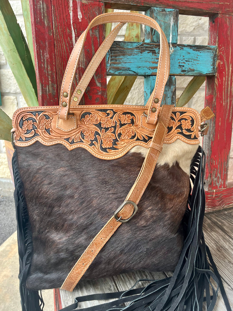 ADBGS143BKW — Front view of women's dark brindle hair-on hide western tote showing espresso brindle cowhide body with white patch, natural tan tooled leather yoke with floral and acanthus scroll tooling on black background, scalloped edge, black fringe sides, and tan adjustable crossbody strap with antique brass buckle — Blair's Western Wear Marble Falls TX