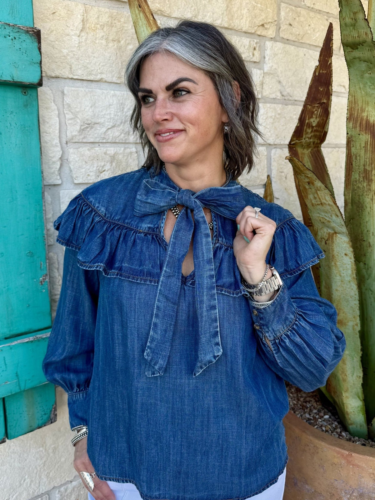630408 — Women's medium denim blue ruffle yoke tie neck long sleeve blouse with double-tiered ruffle yoke across shoulders, keyhole neckline, long self-tie bow, and blouson sleeves with elasticized cuffs — Blair's Western Wear Marble Falls TX