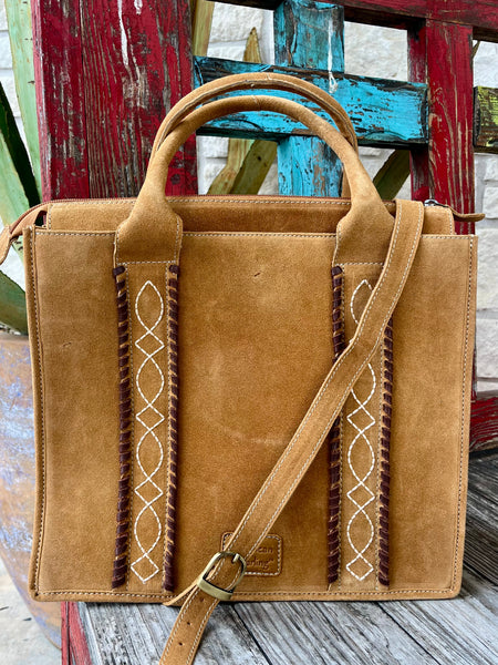 ADBGA605 — Women's golden tan/camel suede structured tote with two vertical dark brown whipstitch leather trim strips and cream/white diamond lattice cross-stitch embroidery on the front panel, two rounded suede top handles, adjustable tan suede crossbody strap with antique gold buckle, top zipper closure, and embossed American Darling logo patch — Blair's Western Wear Marble Falls TX