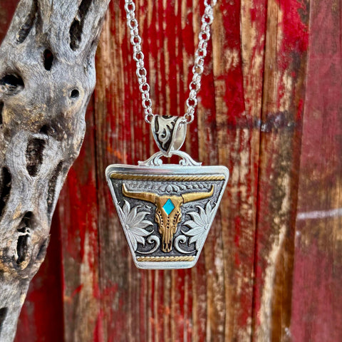 Women’s Montana Silversmiths necklace silver/gold steer-skull pendant in two-tone finish, featuring a turquoise-colored stone accent, with engraved floral detailing – NC5898RTG. Available at Blair's Western Wear, Marble Falls, TX.