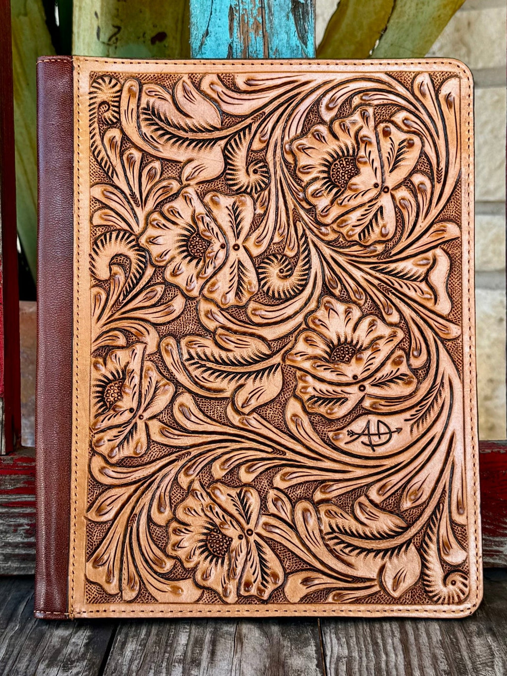 This stunning natural tan leather portfolio is jaw-dropping from the first glance — completely covered in deep hand-carved floral, poppy, and scroll tooling with dark brown antiqued contrast, dark brown leather spine, and American Darling brand stamp on the front