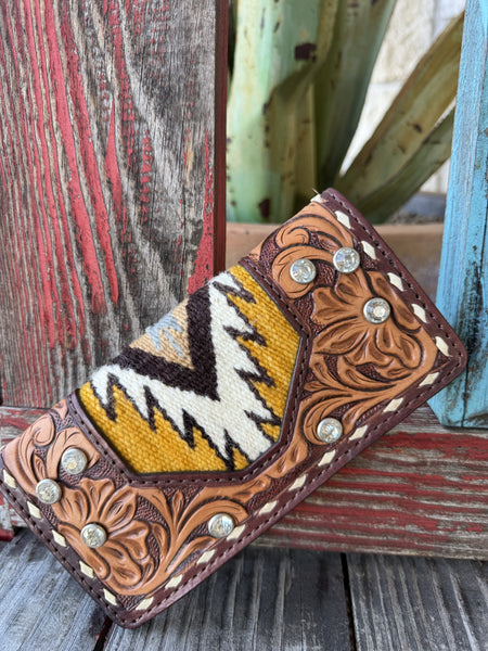 Women's natural tan leather wallet with floral scroll tooling, Aztec-inspired woven blanket inlay in golden yellow, dark brown and cream chevron pattern, crystal rhinestone studs, and cream whipstitch border — Blair's Western Wear Marble Falls TX