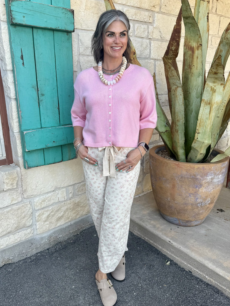 IP200317-03 — Women's natural cream and pink floral barrel leg pant with tie bow waistband, rounded barrel silhouette, horizontal knee seam detail, and cropped ankle length, styled with pink crop cardigan, stacked silver and pearl necklaces, and taupe clogs — Blair's Western Wear Marble Falls TX