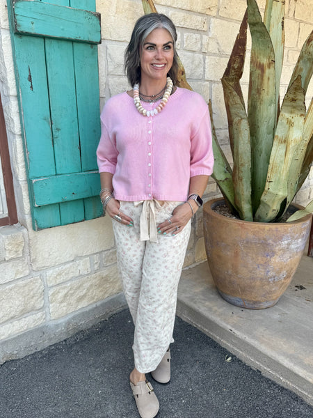 IP200317-03 — Women's natural cream and pink floral barrel leg pant with tie bow waistband, rounded barrel silhouette, horizontal knee seam detail, and cropped ankle length, styled with pink crop cardigan, stacked silver and pearl necklaces, and taupe clogs — Blair's Western Wear Marble Falls TX