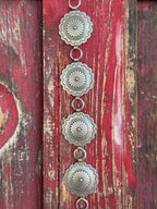 Stacked round silver conchos with deeply stamped sunburst and floral engraving, linked by open rings — this belt carries the weight of real Western artistry. The scalloped edges and layered detailing give it a heritage feel that pairs effortlessly with everything from denim to dresses