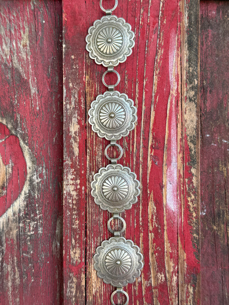 Stacked round silver conchos with deeply stamped sunburst and floral engraving, linked by open rings — this belt carries the weight of real Western artistry. The scalloped edges and layered detailing give it a heritage feel that pairs effortlessly with everything from denim to dresses