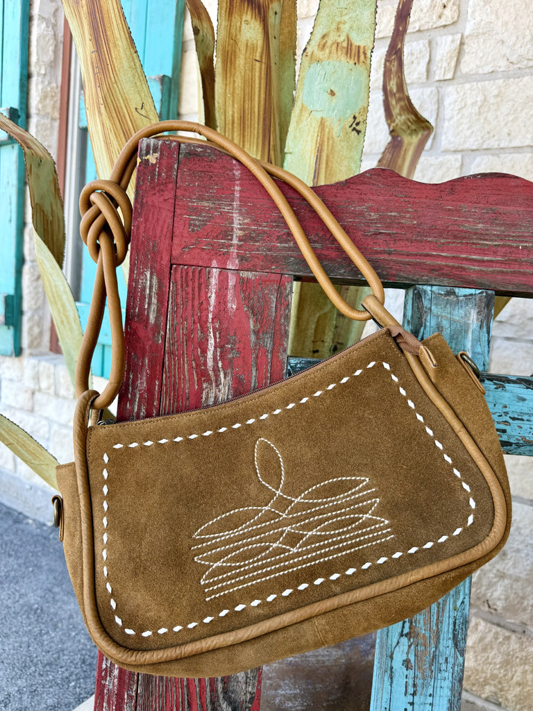 Women's tan suede leather crossbody purse with white whipstitch border, decorative cross-stitch embroidery, and knotted leather strap detail — Blair's Western Wear Marble Falls TX