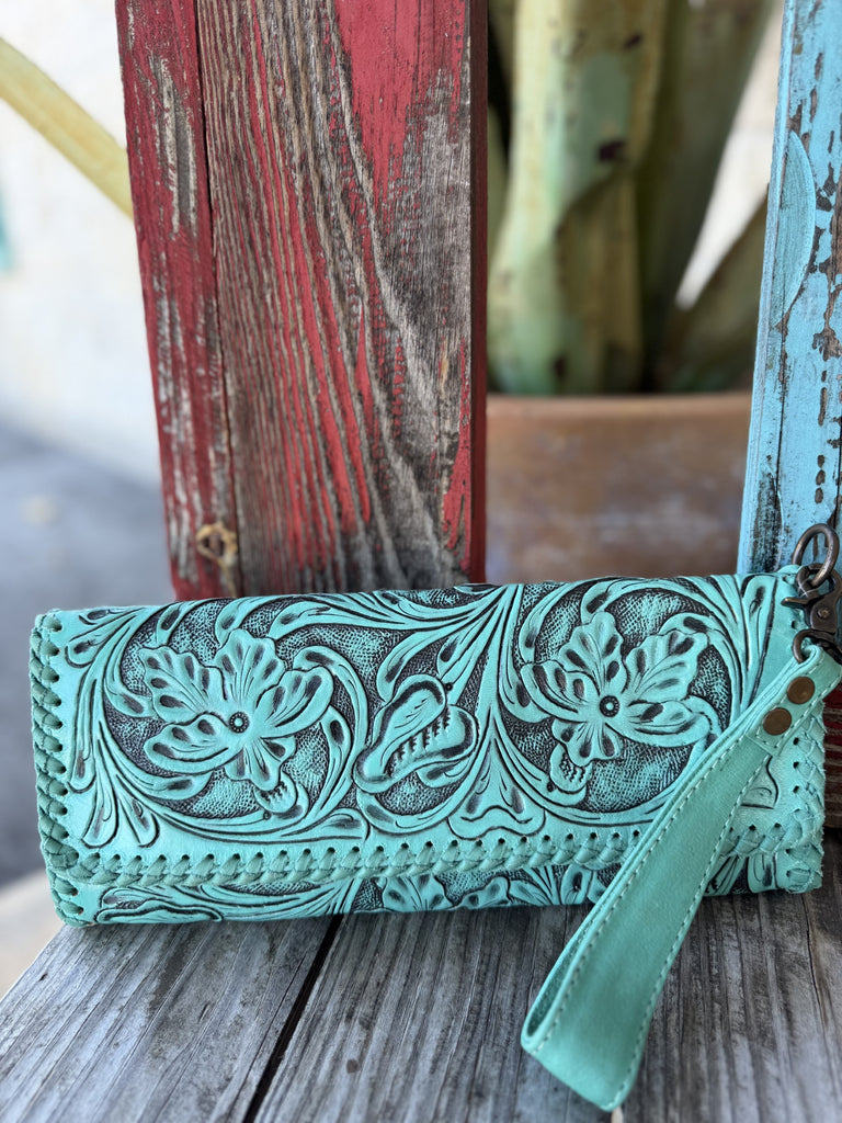 This stunning turquoise hand-tooled leather wristlet clutch is pure western artisan magic — deep floral and scroll carving with rich dark antiqued contrast, punched hole edge detailing, and a turquoise leather wrist strap with gunmetal hardware — Blair's Western Wear Marble Falls TX