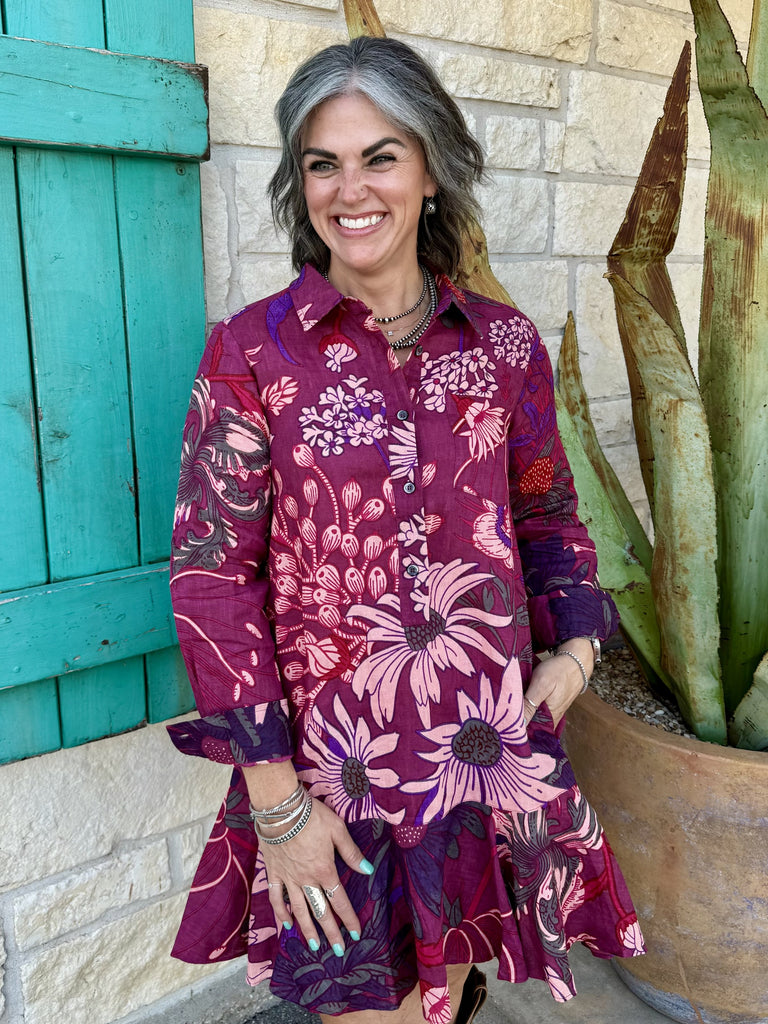 72688 — Women's deep wine burgundy oversized floral linen swing shirt dress with large pink dahlias, echinacea, and hydrangea botanical print, point collar, button-front placket, long sleeves with button cuffs, drop-waist silhouette, and dramatically flared swing skirt, styled with tall brown western boots — Blair's Western Wear Marble Falls TX
