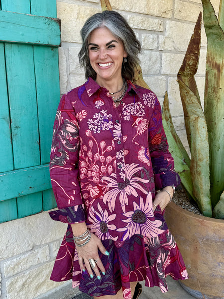 72688 — Women's deep wine burgundy oversized floral linen swing shirt dress with large pink dahlias, echinacea, and hydrangea botanical print, point collar, button-front placket, long sleeves with button cuffs, drop-waist silhouette, and dramatically flared swing skirt, styled with tall brown western boots — Blair's Western Wear Marble Falls TX