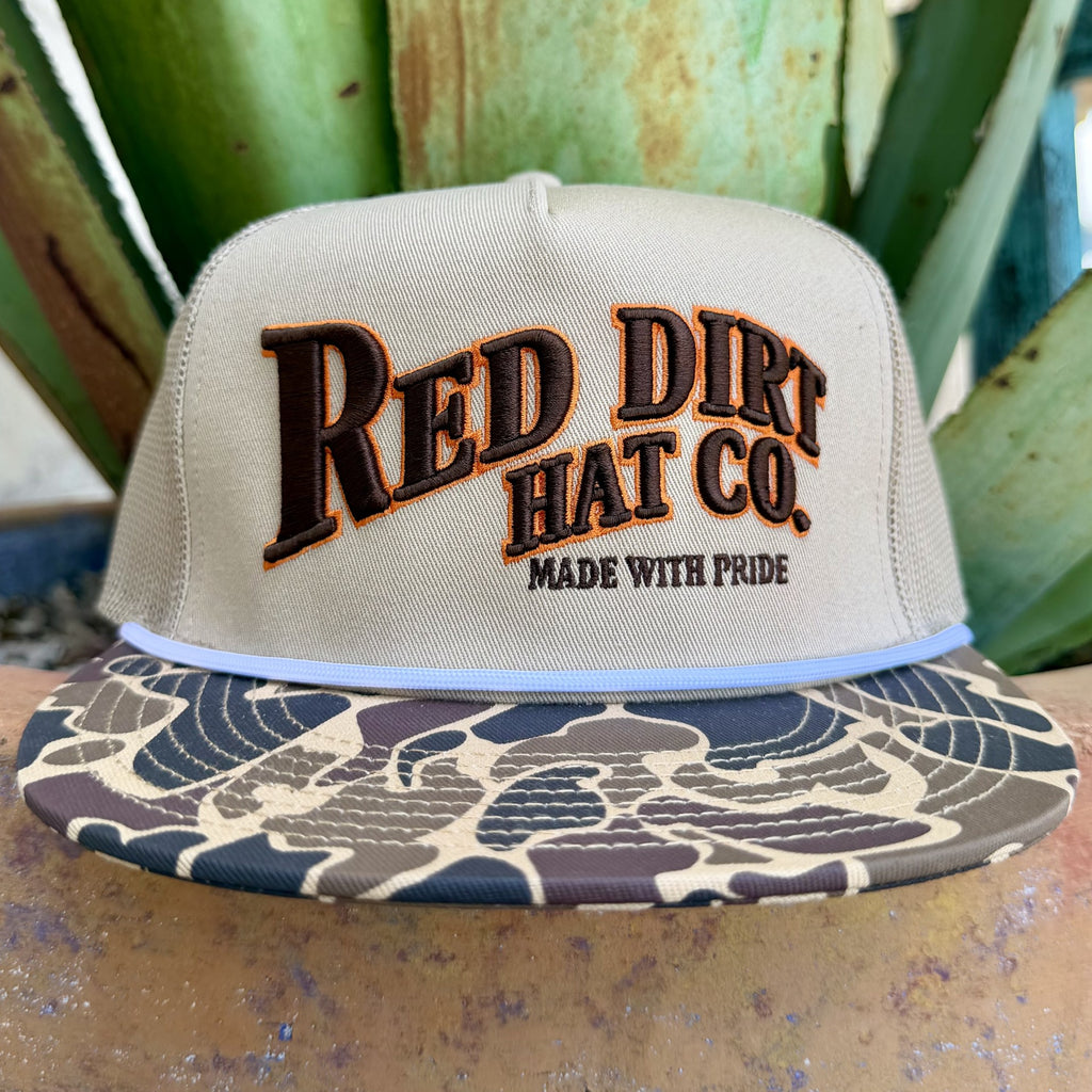 Men's tan mesh trucker cap with embroidered Red Dirt Hat Co. logo and camo bill with orange accents — Blair's Western Wear Marble Falls TX