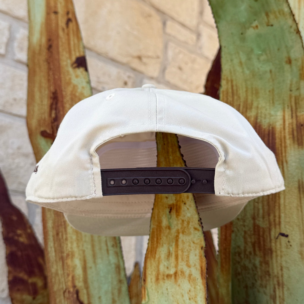 An off-white snapback cap shown from the back, featuring a brown plastic adjustment strap