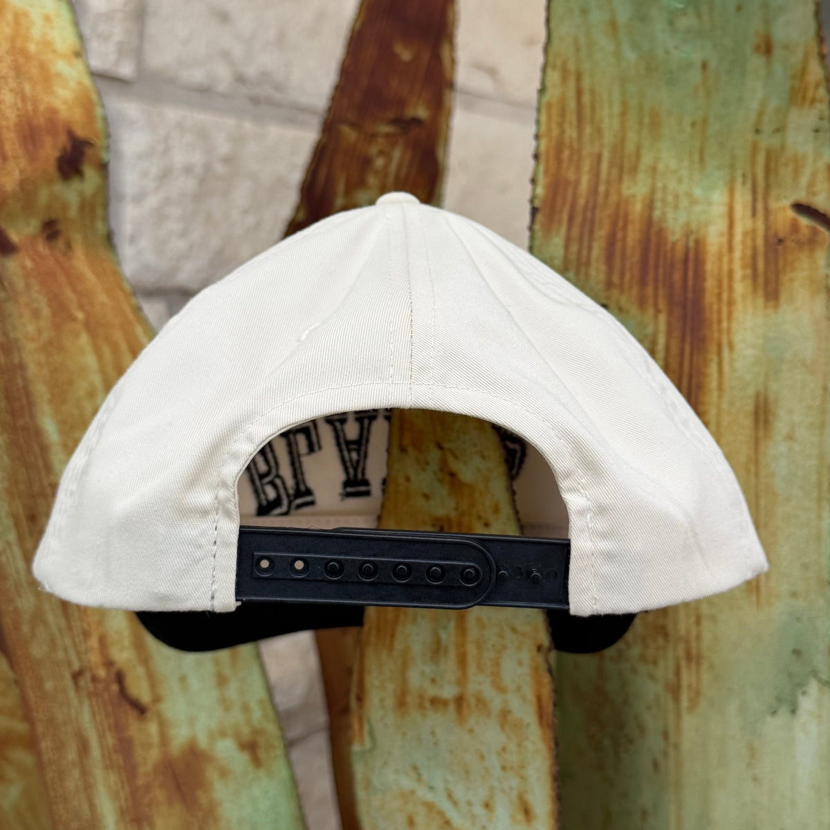 The back of an off white snapback cap with a black adjustable strap
