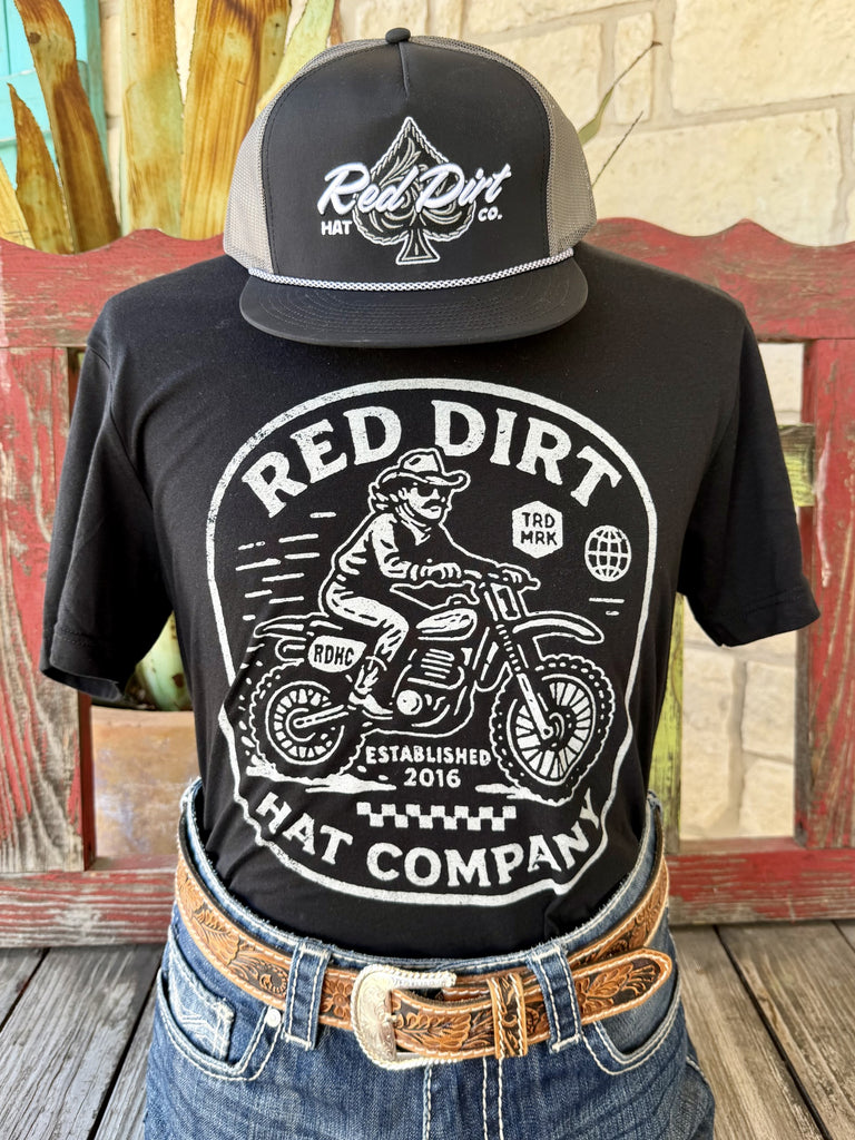 Men's black Red Dirt Hat Co. Motorcycle short sleeve tee with bold white cowboy on dirt bike Established 2016 badge front graphic, front view styled with jeans and tooled leather belt — Blair's Western Wear Marble Falls TX