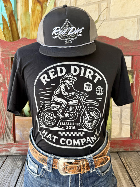 Men's black Red Dirt Hat Co. Motorcycle short sleeve tee with bold white cowboy on dirt bike Established 2016 badge front graphic, front view styled with jeans and tooled leather belt — Blair's Western Wear Marble Falls TX