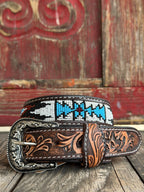 Dark leather is hand-tooled with golden floral scrollwork and inlaid with a vivid Aztec-inspired beaded stripe in cobalt blue, burgundy, and white — finished with an ornate engraved silver buckle for a bold southwestern statement. Available at BLAIR'S Western Wear located in Marble Falls TX 