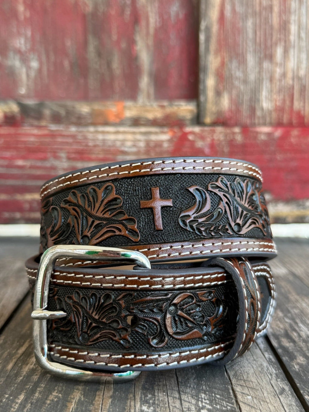 Leather Western belt featuring a hand-tooled floral pattern with a textured black background and a centered cross design. Finished with double white contrast stitching, matching leather keeper, and a polished silver roller buckle. Built for everyday wear with durable leather construction and classic Western craftsmanship.

Available at Blairs' Western Wear, located in Marble Falls.