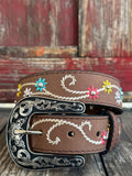 A brown leather belt with white embroidered swirls and colorful floral details, featuring a large engraved silver buckle, displayed on a rustic wooden surface. Available at BLAIR'S Western Wear located in Marble Falls TX 