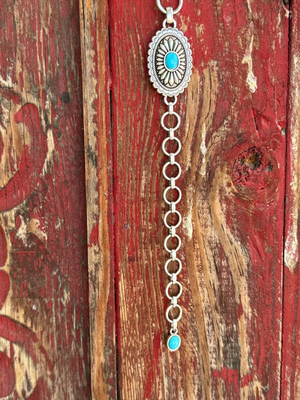A1308233 — Kid's Turquoise Concho Chain Western Belt Full silver concho chain belt with repeating oval silver conchos featuring engraved petal/sunburst detail, rope edge border, and turquoise stone center in each. Silver O-ring links connect each concho. Adjustable silver O-ring chain tail with small turquoise stone drop tip. Available at Blair's Western Wear located in Marble Falls TX 