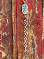A1308233 — Kid's Turquoise Concho Chain Western Belt Full silver concho chain belt with repeating oval silver conchos featuring engraved petal/sunburst detail, rope edge border, and turquoise stone center in each. Silver O-ring links connect each concho. Adjustable silver O-ring chain tail with small turquoise stone drop tip. Available at Blair's Western Wear located in Marble Falls TX 