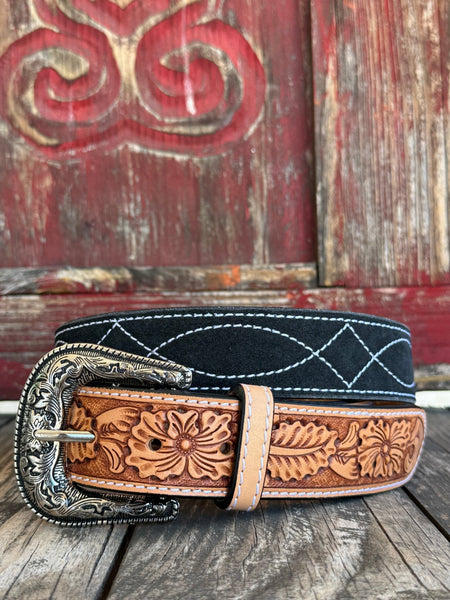 A striking two-tone belt combining a black suede upper panel with a tan hand-tooled floral leather lower panel, finished with white edge stitching and an ornate silver floral scroll buckle with rope-edge border. Bold contrast, artisan detail, and undeniable Western character. Shop at Blair's Western Wear — blairswesternwear.com.