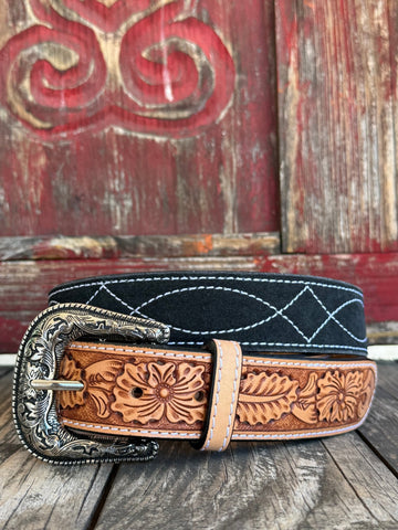 A striking two-tone belt combining a black suede upper panel with a tan hand-tooled floral leather lower panel, finished with white edge stitching and an ornate silver floral scroll buckle with rope-edge border. Bold contrast, artisan detail, and undeniable Western character. Shop at Blair's Western Wear — blairswesternwear.com.