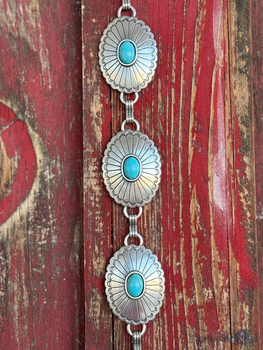 A fully linked silver concho chain belt featuring large oval conchos with intricate stamped sunburst detailing and a vibrant turquoise center stone in each — connected by silver rings throughout for an adjustable, flexible fit - timeless, southwestern-inspired western belt that adds instant color and character to jeans, dresses, or tunics.
