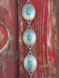 A fully linked silver concho chain belt featuring large oval conchos with intricate stamped sunburst detailing and a vibrant turquoise center stone in each — connected by silver rings throughout for an adjustable, flexible fit - timeless, southwestern-inspired western belt that adds instant color and character to jeans, dresses, or tunics.