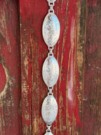 A fully linked silver concho chain belt featuring large oval conchos with intricate etched scroll and floral engraving throughout, connected by silver rings for an adjustable, flexible fit. All-silver, all-Western, and effortlessly elegant. Shop at Blair's Western Wear — blairswesternwear.com.