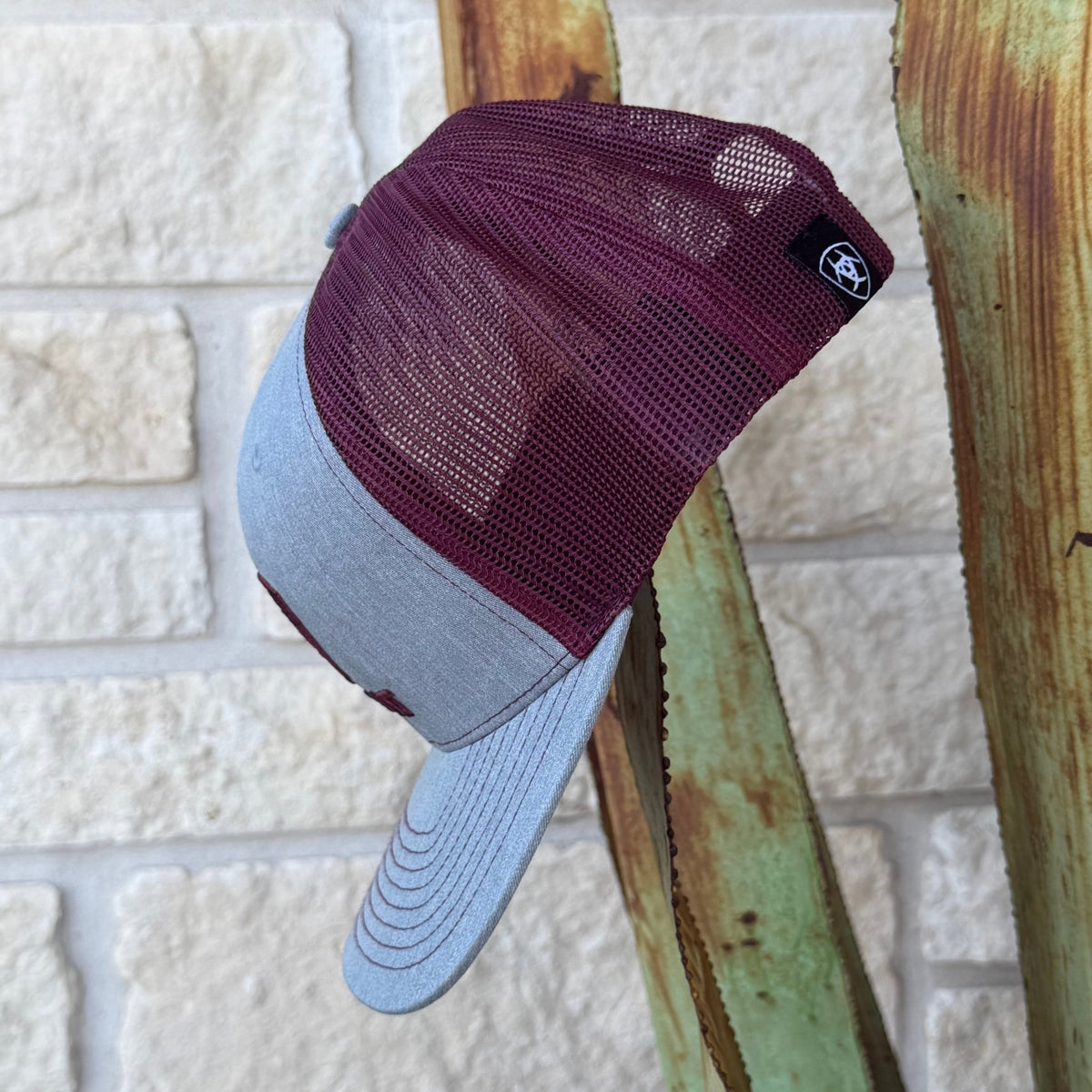 A two-tone trucker cap with a maroon mesh back and a light gray fabric brim, 