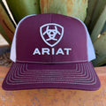 A maroon and white trucker hat with white embroidered Ariat logo and text, 