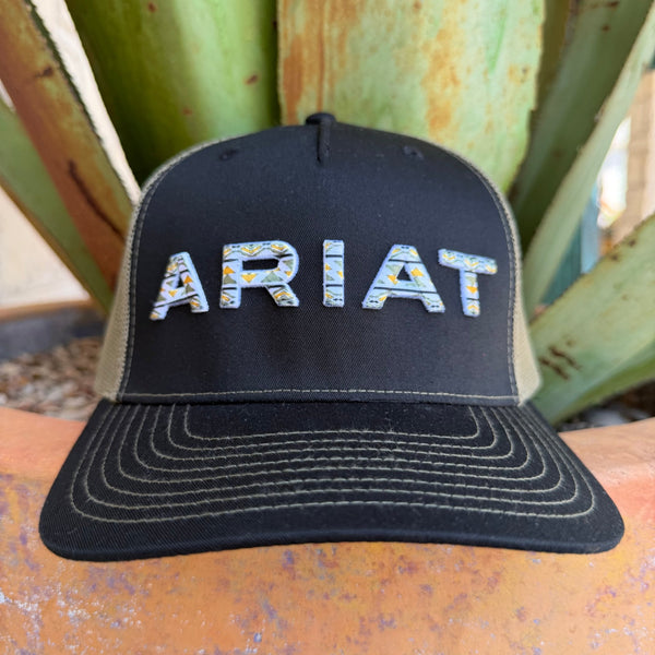 A black trucker-style cap with olive mesh side panels and a curved brim, featuring the word ARIAT embroidered across the front in a white, green, and yellow pattern.