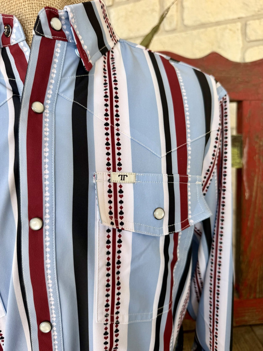 Close-up of men's light blue and wine striped snap shirt showing miniature playing-card suit motifs, Western yoke stitching, pointed pocket flap, and light-colored snaps — Blair's Western Wear Marble Falls TX