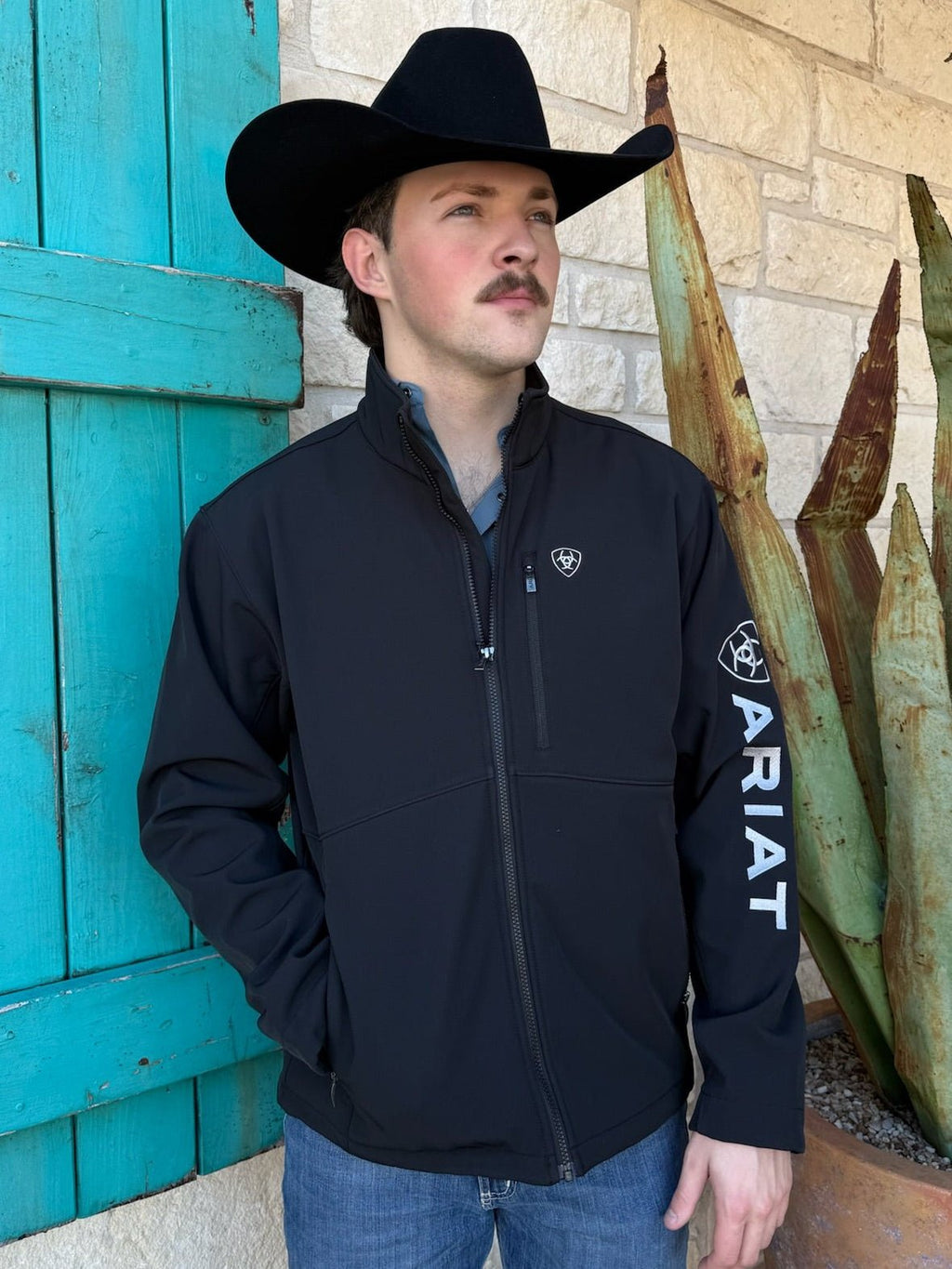 Men’s Ariat softshell jacket in black, wind- and water-resistant stretch fabric, fleece-lined for warmth, with zip pockets and Ariat logo on sleeve - 10062578. Available at Blair’s Western Wear, Marble Falls, TX.