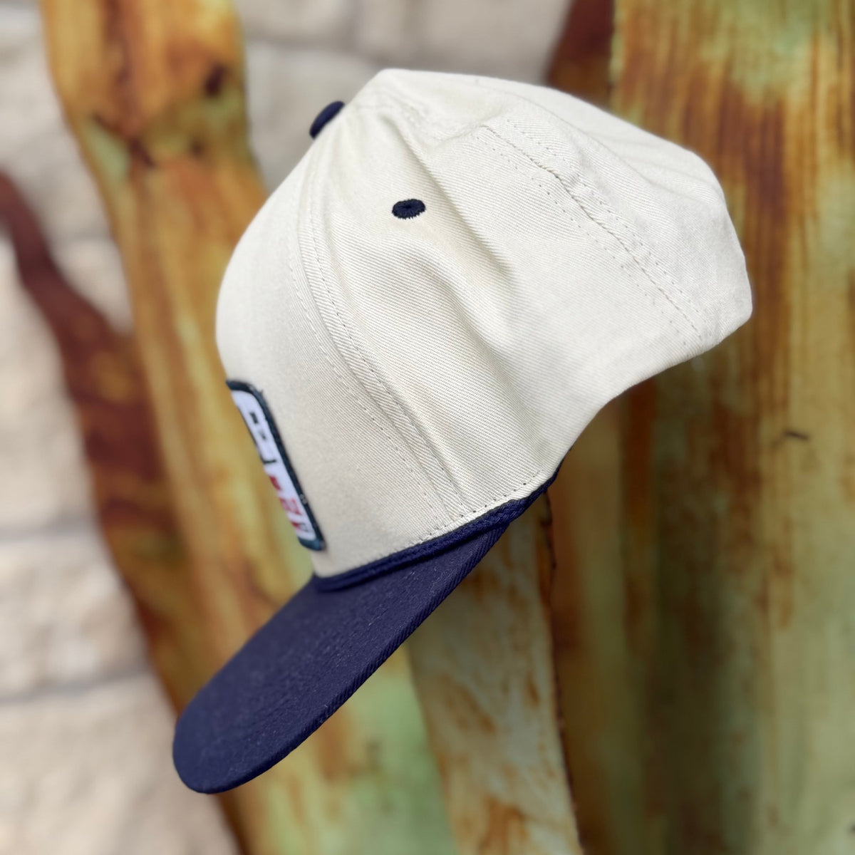 A structured cap with an off-white crown and a dark navy blue flat brim, 
