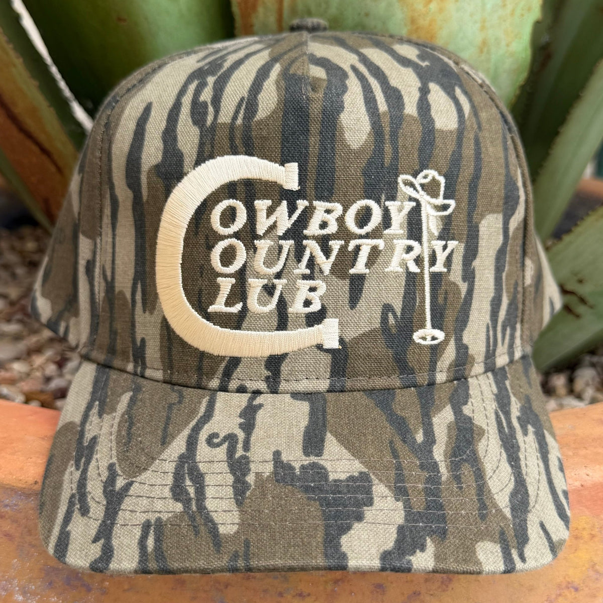 A camouflage cap with 'COWBOY COUNTRY CLUB' and a cowboy hat graphic in white on the front