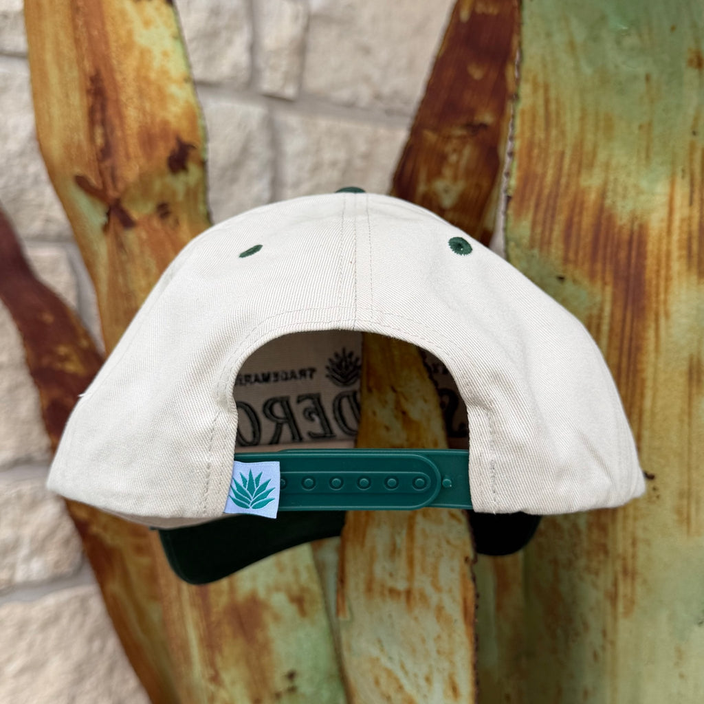 The back of a light beige snapback cap with a dark green adjustable strap and a small white brand tag featuring the Sendero logo. 