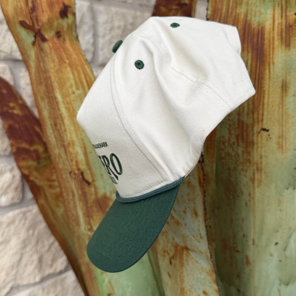 An off-white baseball cap with a dark green visor and matching green eyelets,