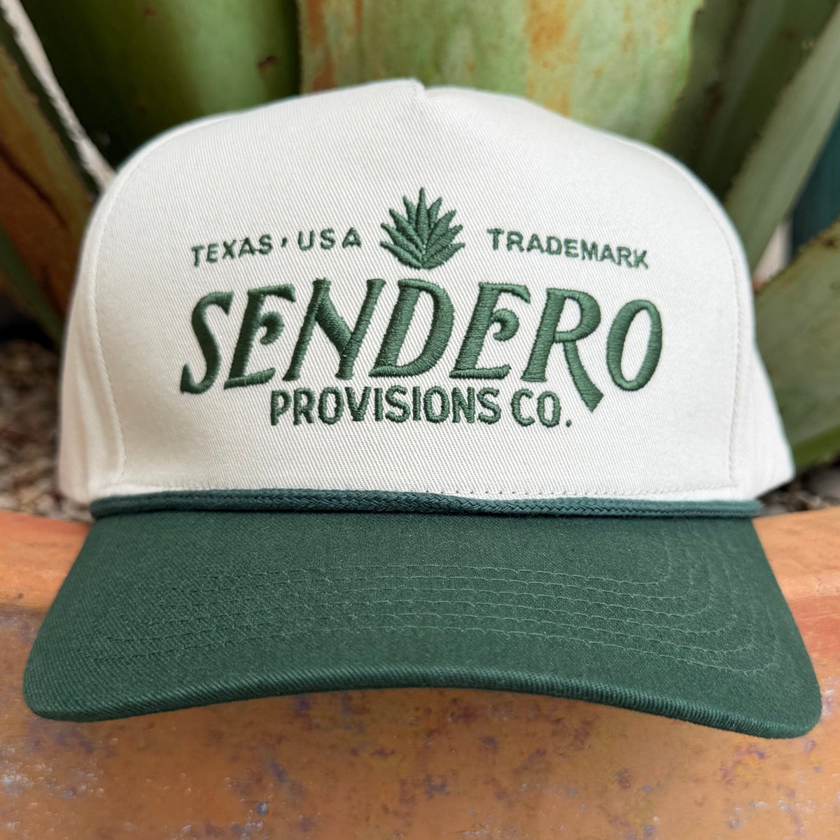 An off-white and dark green trucker-style cap with 'SENDERO PROVISIONS CO.' embroidered on the fron