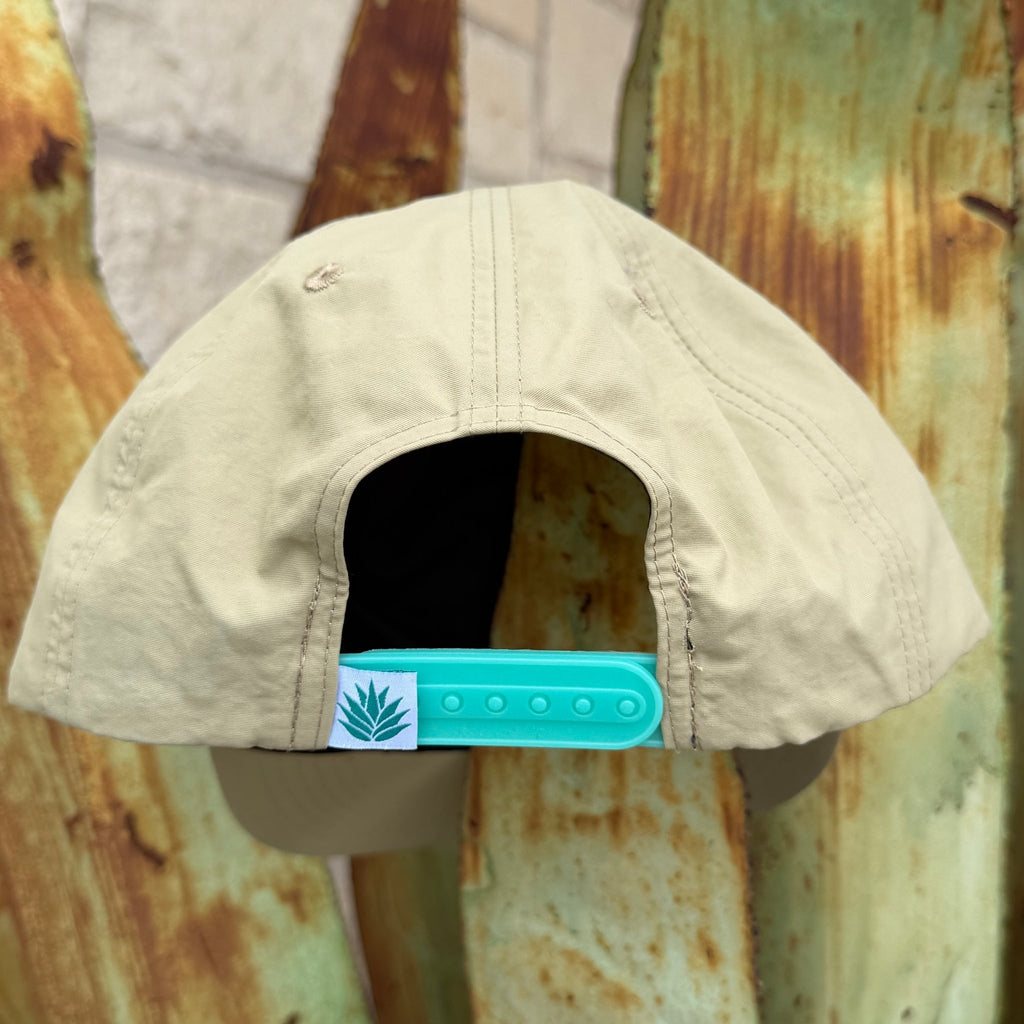 A beige cap viewed from the back, featuring a turquoise snapback closure with a small white square patch printed with the Sendero logo 