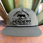 An olive green cap with a black embroidered graphic reading 'THE TALE OF CHUPACABRA SENDERO PROVISIONS CO. 2014' and a chupacabra silhouette