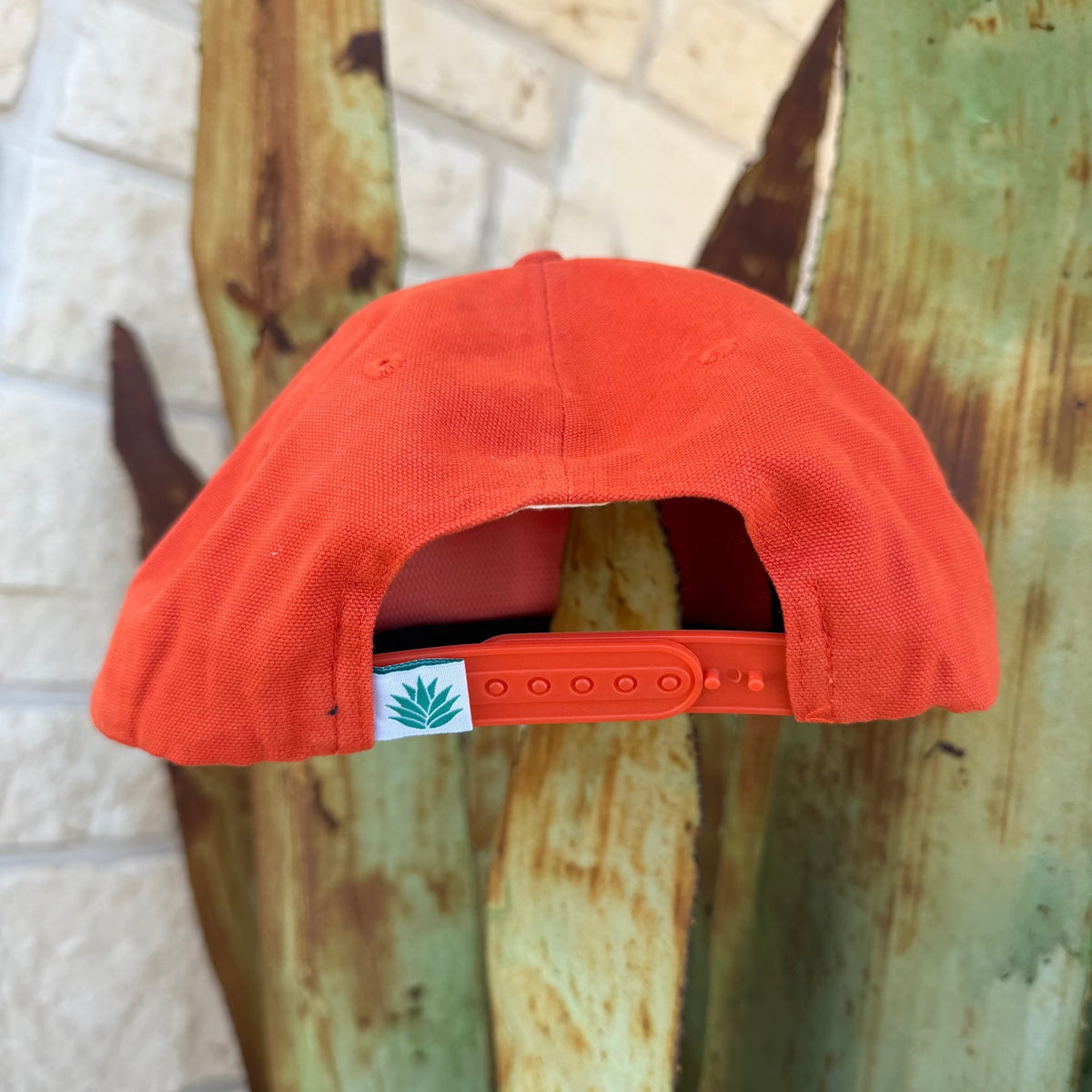 An orange snapback cap shown from the back, featuring a small white brand tag with the sendero logo and orange adjustment strap