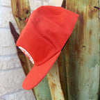An orange snapback cap with a white circular patch on the front
