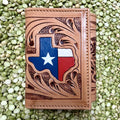 Natural tan leather trifold wallet with a Texas-shaped red, white, and blue flag accent, white star, dark floral-scroll tooling, and stitched borders — Blair's Western Wear Marble Falls TX