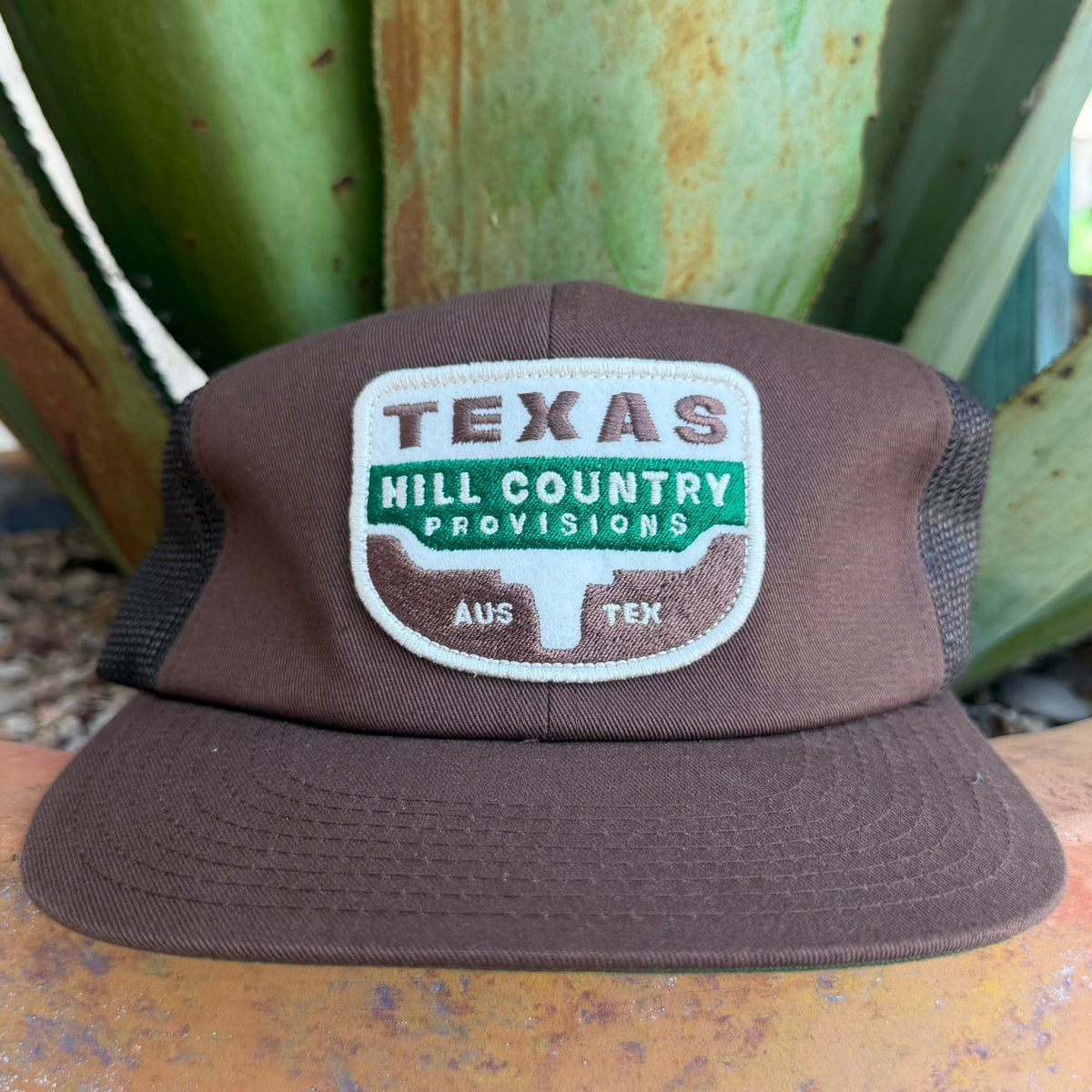 A brown cap with a mesh back and a front patch reading 'TEXAS HILL COUNTRY PROVISIONS AUS TEX', 