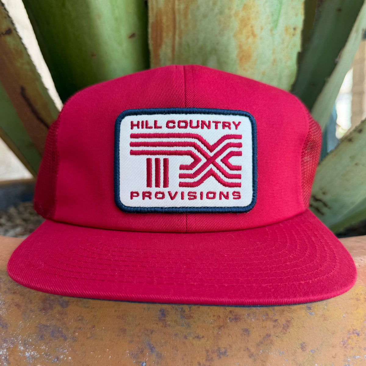 A bright red cap with a white rectangular front patch reading 'HILL COUNTRY PROVISIONS' and a red logo, 