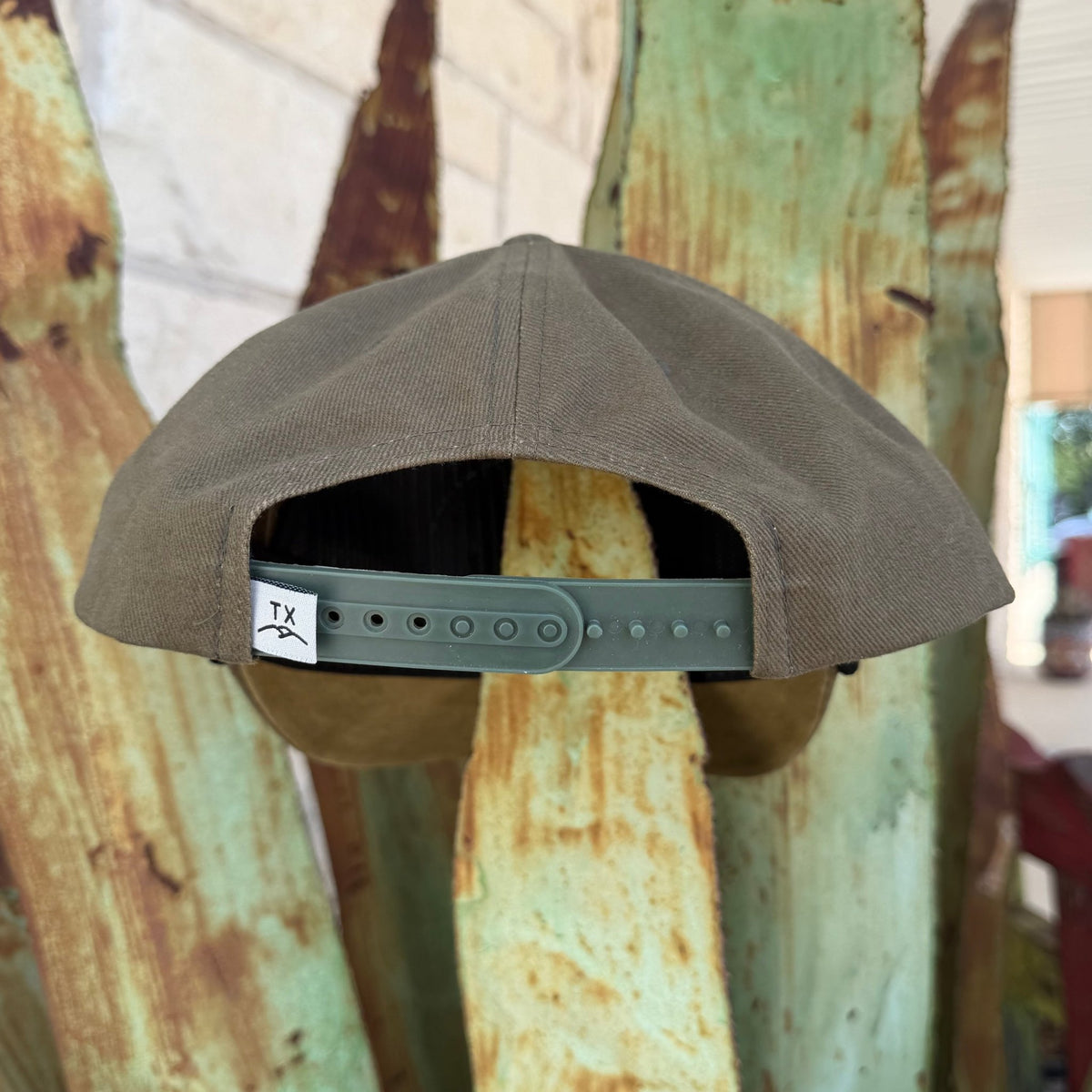An olive structured snapback cap shown from the back. The cap features a green adjustable strap with a white brand tag that reads 'TX'.