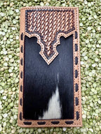 A rectangular leather wallet or card holder with a tan woven-texture top panel, decorative cutout border, and a black-and-white cowhide center, photographed from above on a bed of green lentils.